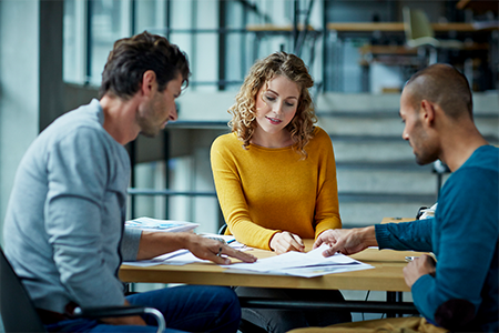 3 business professionals collaborating at a desk, looking at papers